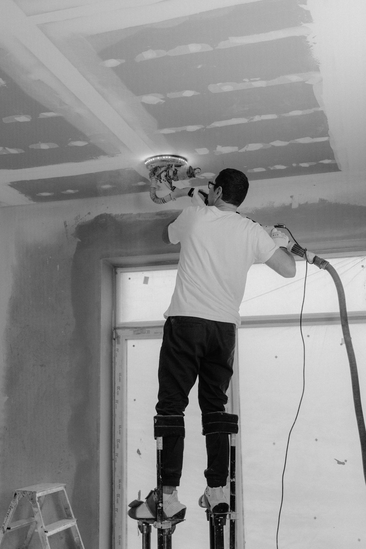 Finisher on stilts sanding a skim-coated drywall ceiling smooth before texture and paint