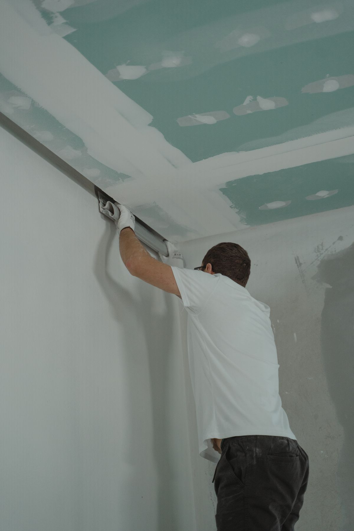 Contractor finishing taped joints where new drywall meets the wall — covering with new drywall is one option for asbestos-positive ceilings